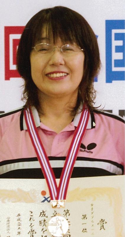 ピンク色のスポーツウエアを着た眼鏡をかけた女性が手には賞状首にはメダルをかけ笑顔の記念写真