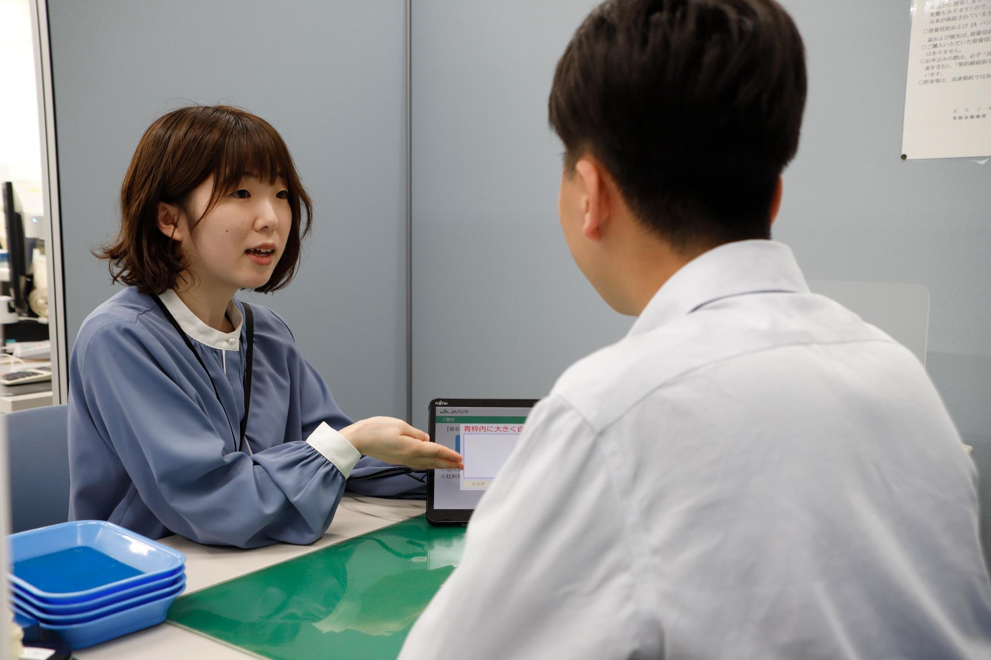 写真：窓口でタブレット端末を使い、顧客に対応する尾崎さん