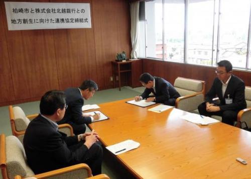 柏崎市と北越銀行の代表が机の上でお互いに協定書にサインをしている写真