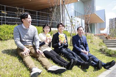写真：元気発信課の移住相談担当の職員4人が市役所前の芝生に並んで座っています。