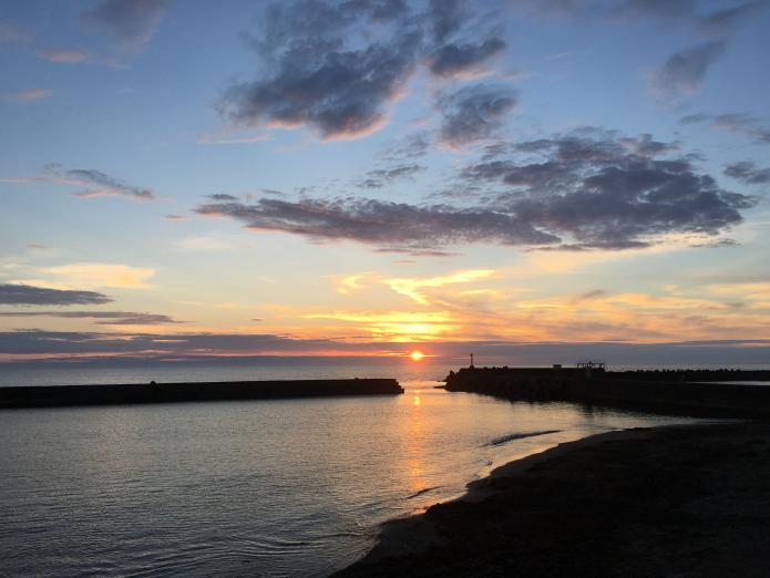 防波堤とテトラポットの間を沈んでいく夕日が小さく見えている写真